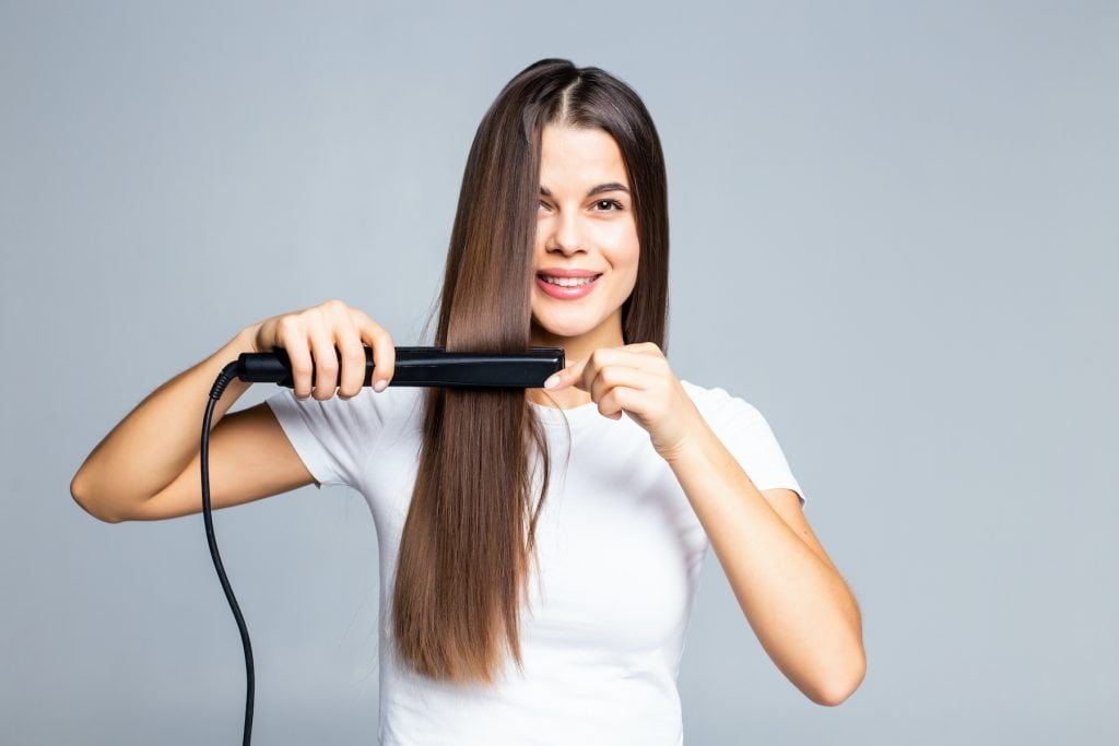 saç düzleştiricisi kullanan uzun saçlı genç kadın